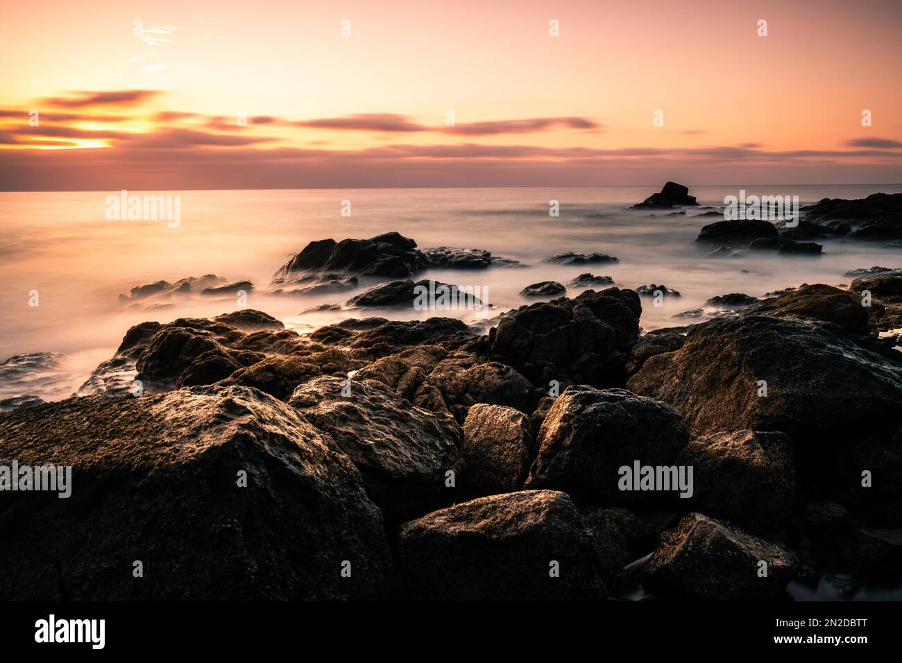 Sunrise, over the sea in a rocky bay, clouds, long exposure, backlight shot, volcanic rock, Fuerteventura, Canary Islands, Spain Stock Photo