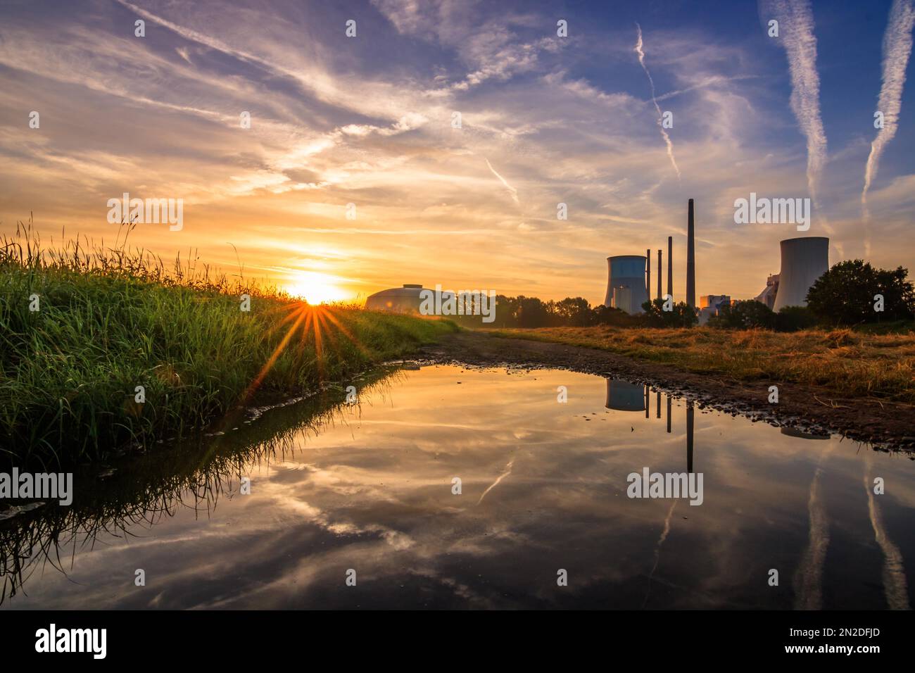 Beautiful sunrise in a field, with a puddle in the sunrise. Backlight shot in the morning, in the background the coal-fired power plant Staudinger Stock Photo