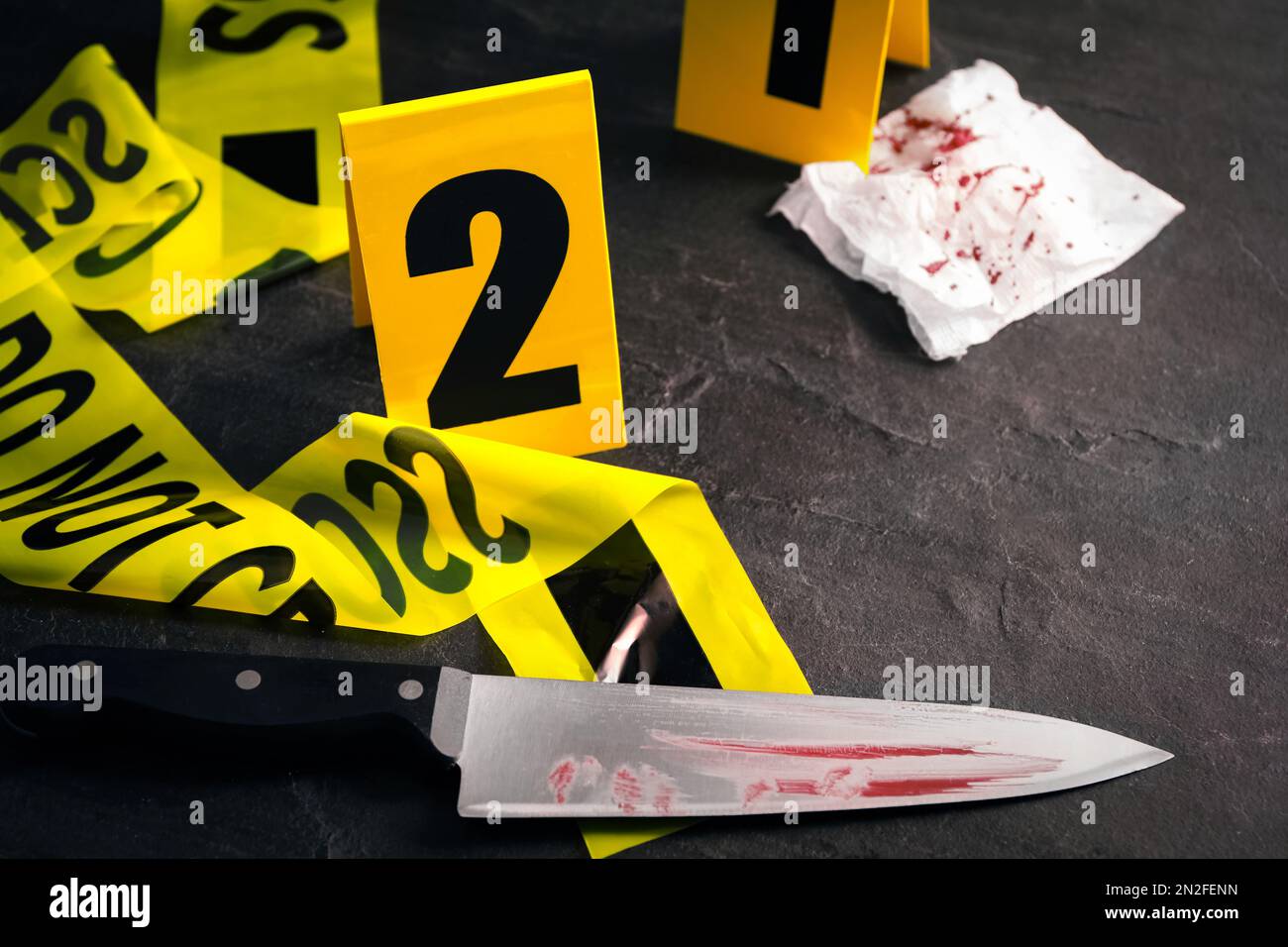 Bloody knife, yellow tape and evidence marker on black slate table