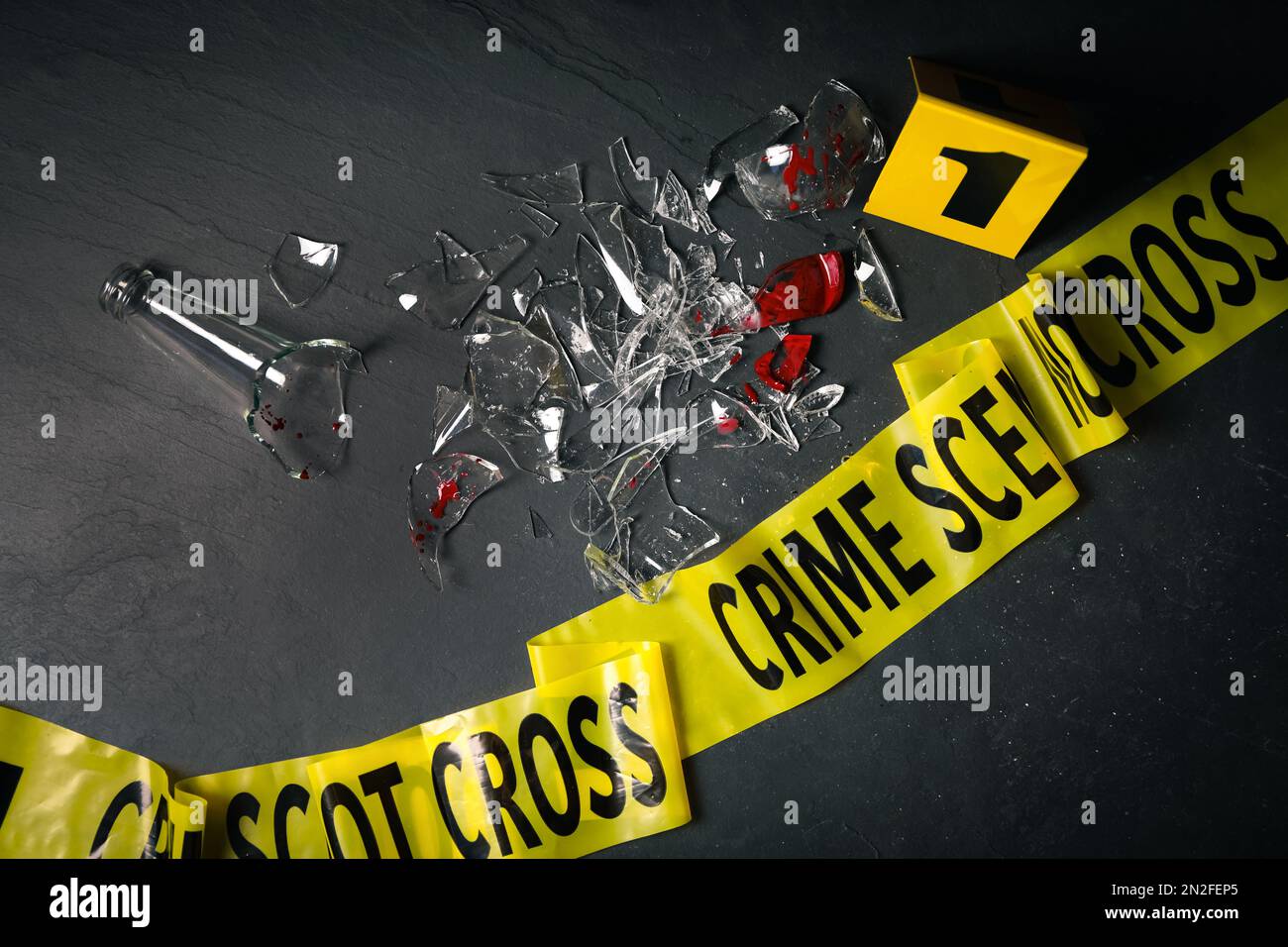 Broken bottle with blood, yellow tape and evidence marker on black