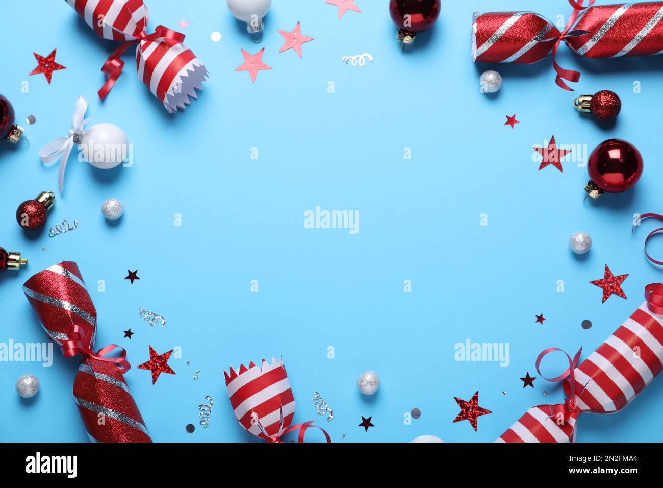 Frame of Christmas crackers and decorations on light blue background, top view with space for text Stock Photo