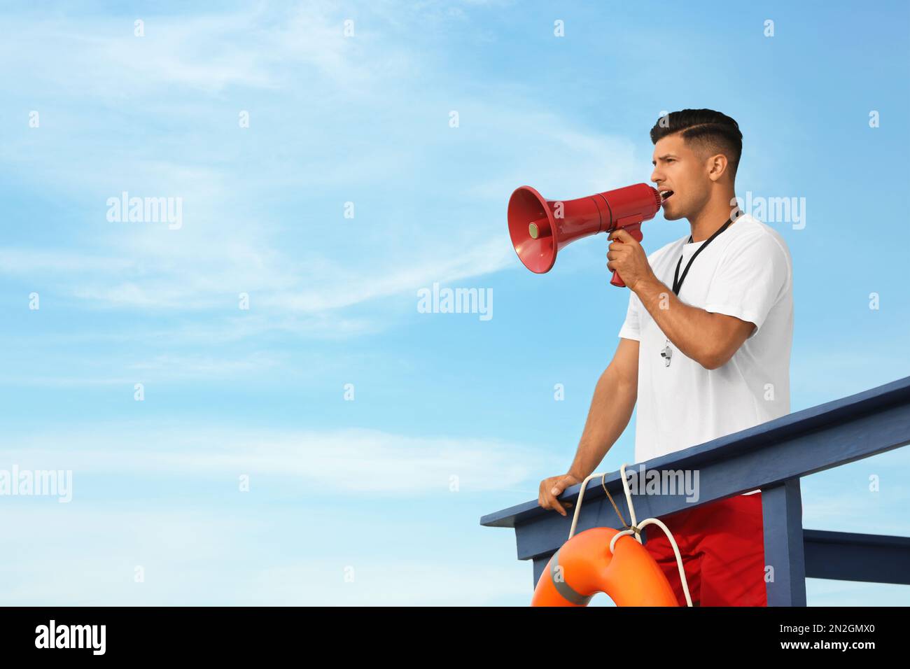 Male lifeguard with megaphone on watch tower against blue sky Stock Photo - Alamy