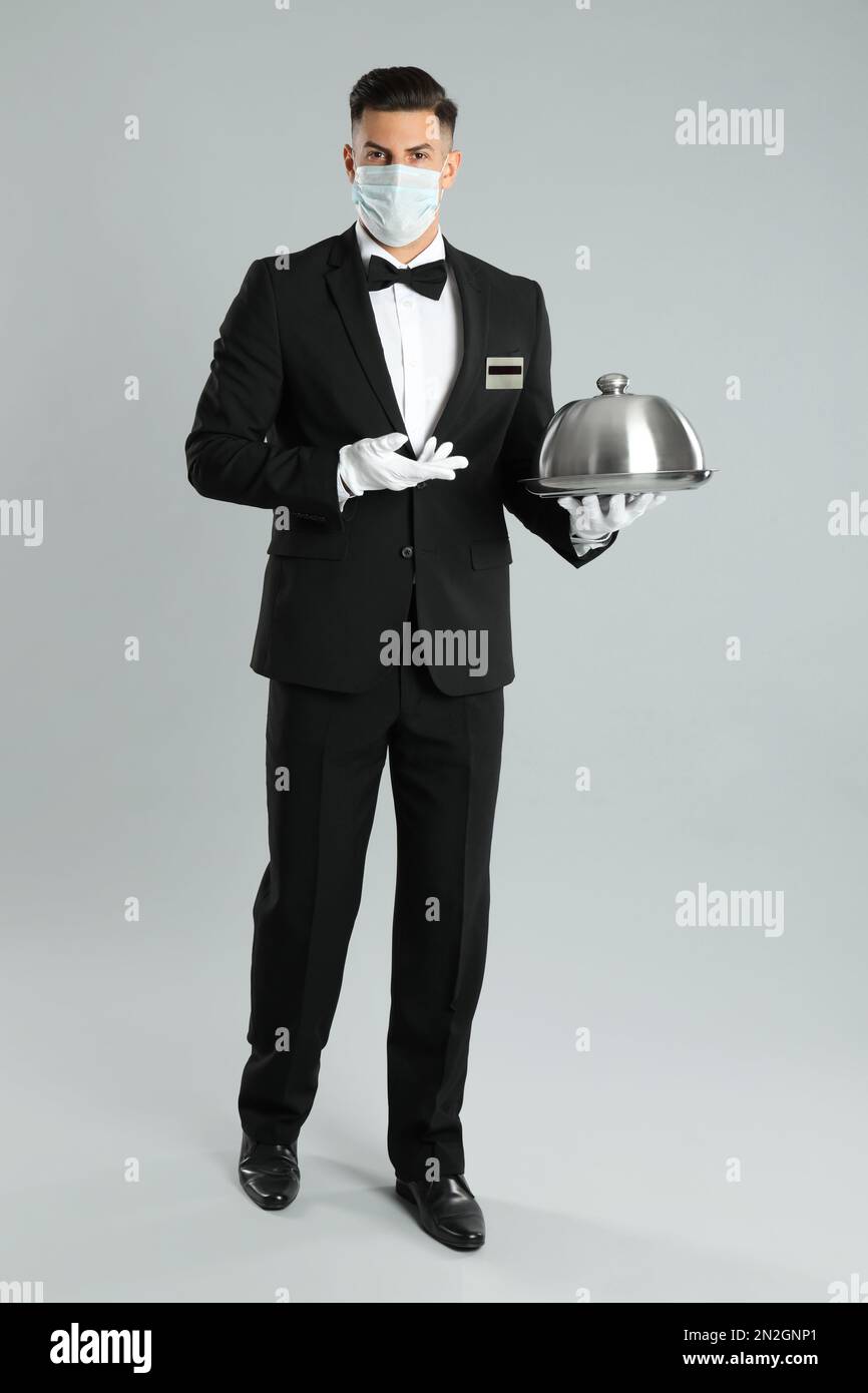 Waiter in medical face mask holding tray on light grey background Stock ...