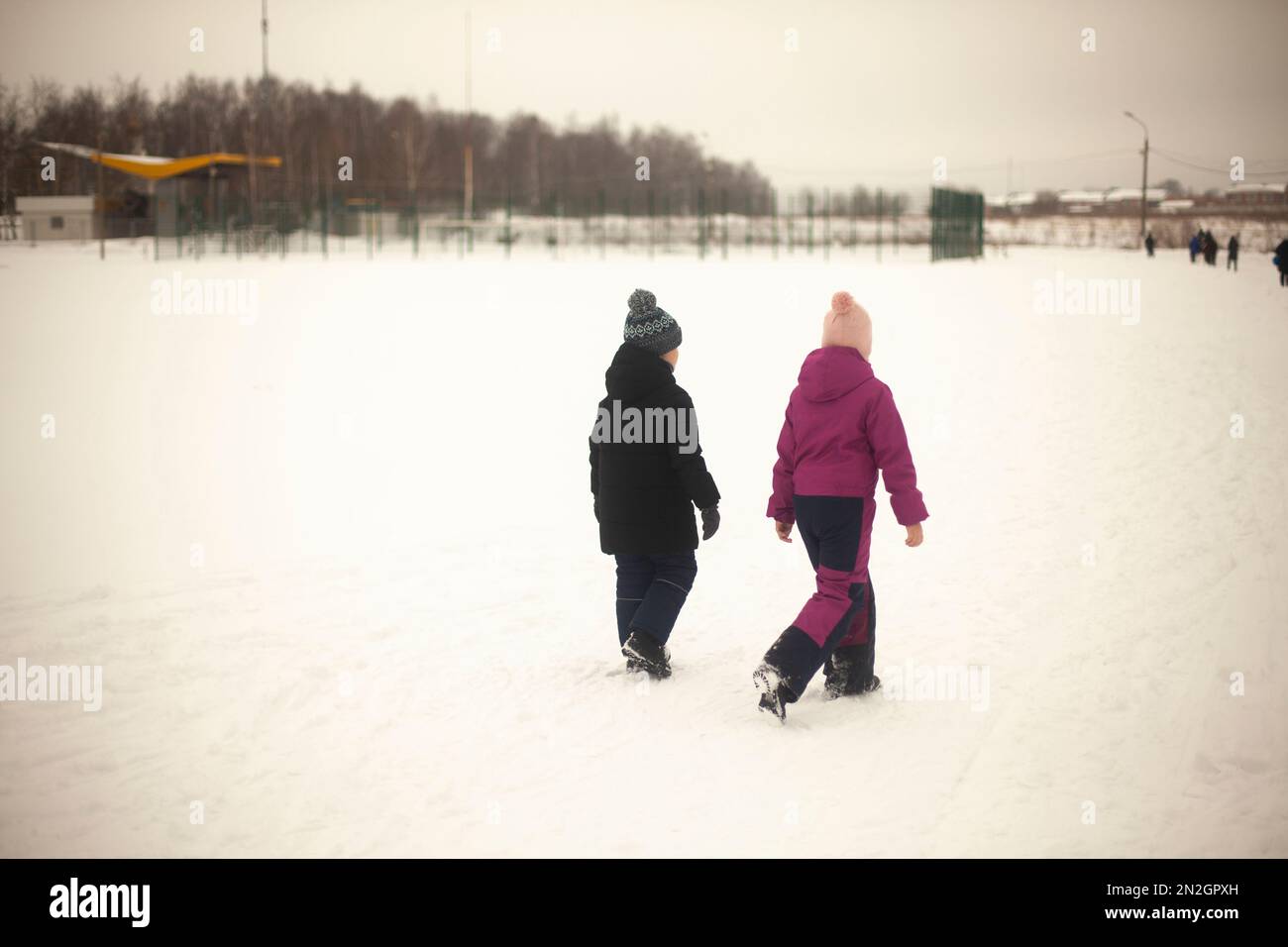 Children walk through snowy field. Children walk outside in winter. Warm clothes in cold weather. Walk down street. Stock Photo
