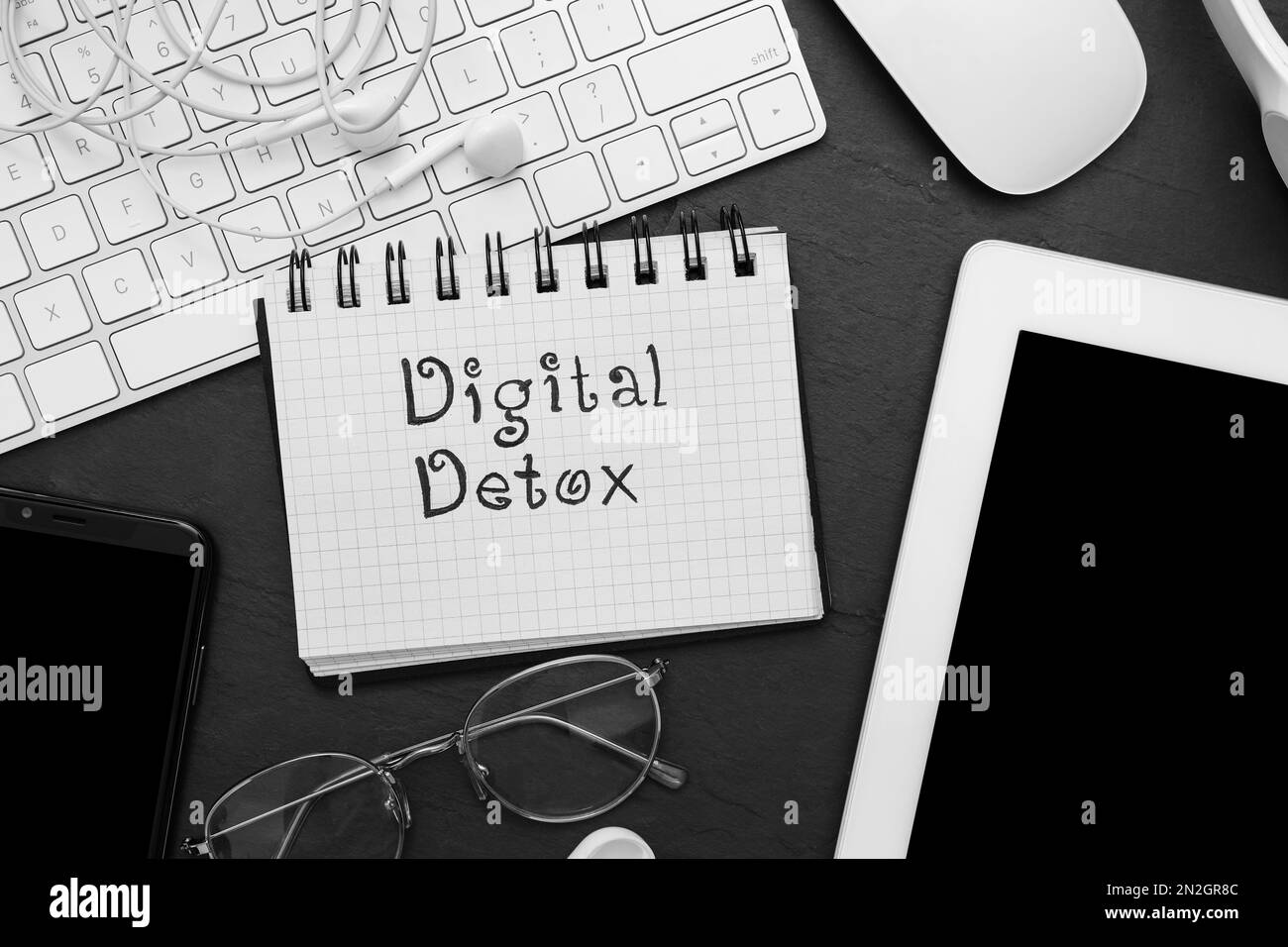 Notebook with phrase DIGITAL DETOX, glasses and different gadgets on black table, flat lay Stock Photo