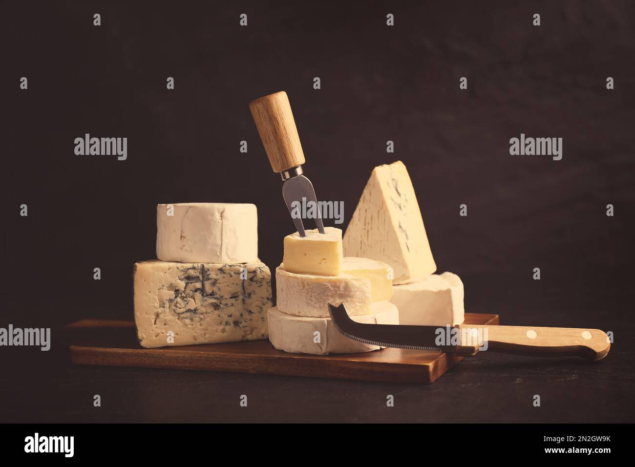 Different types of cheese, knife and fork on black table Stock Photo