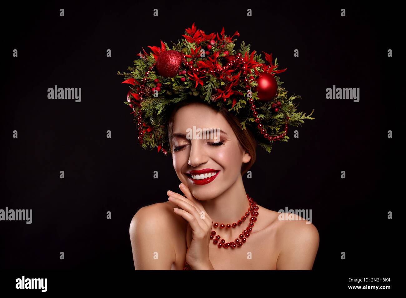 Beautiful young woman wearing Christmas wreath on black background Stock Photo