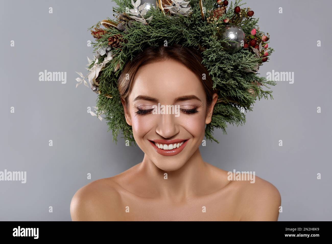 Beautiful young woman wearing Christmas wreath on grey background Stock Photo