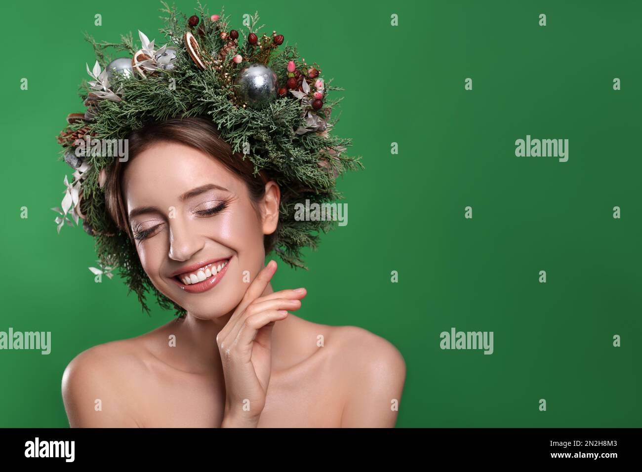 Beautiful young woman wearing Christmas wreath on green background. Space for text Stock Photo