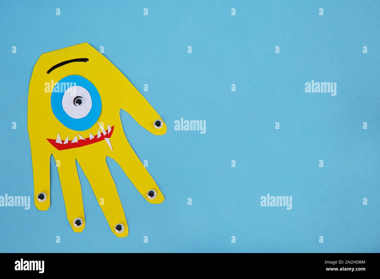 Funny yellow hand shaped monster on light blue background, top
