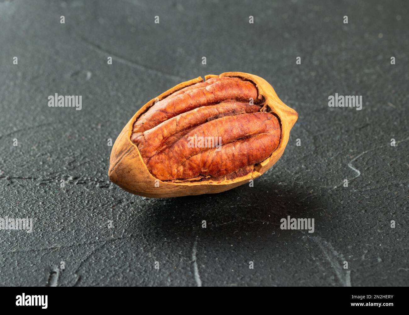 Cracked in-shell pecan close-up on dark concrete background Stock Photo