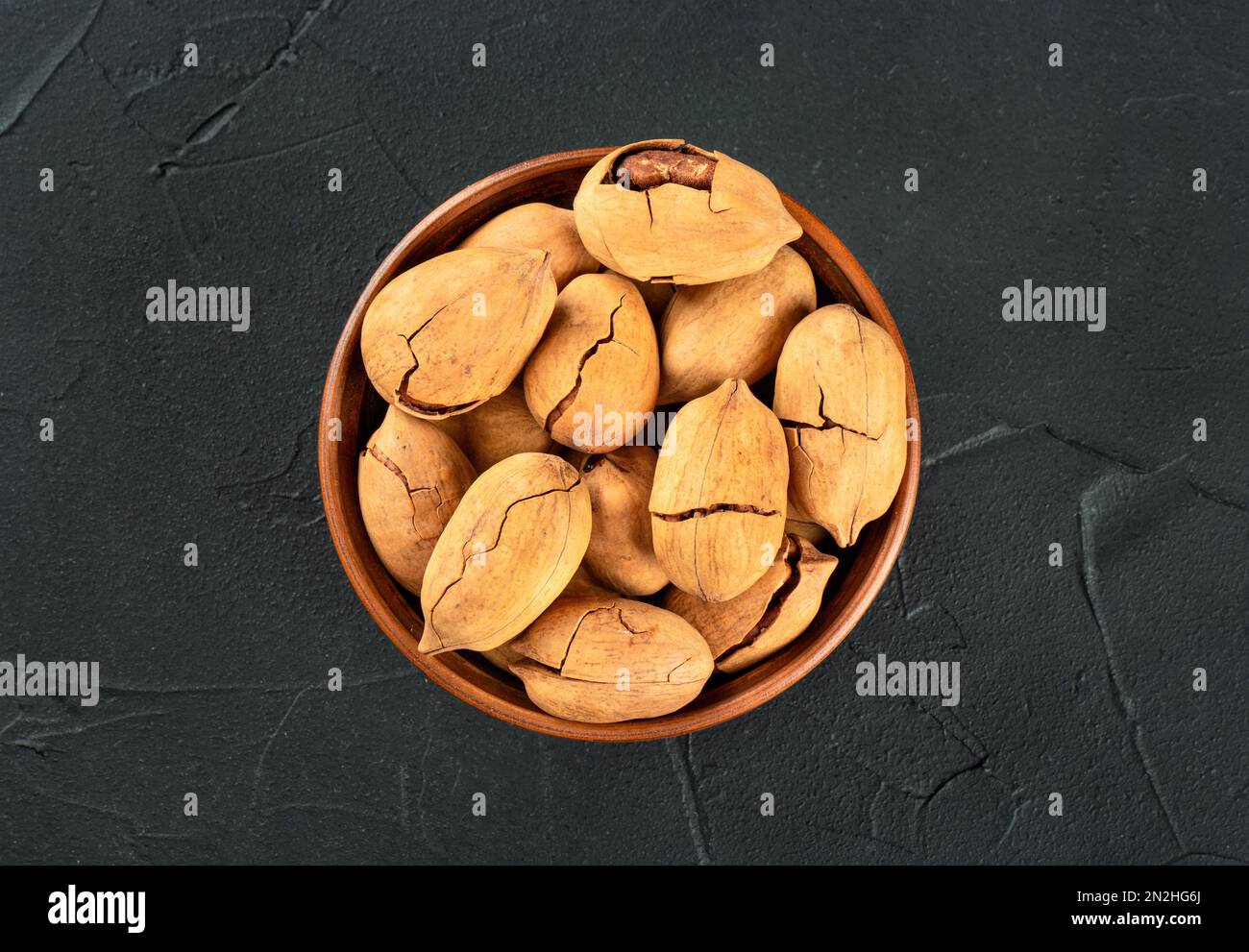 Pecan nuts in a bowl on a dark concrete background, top view. Stock Photo