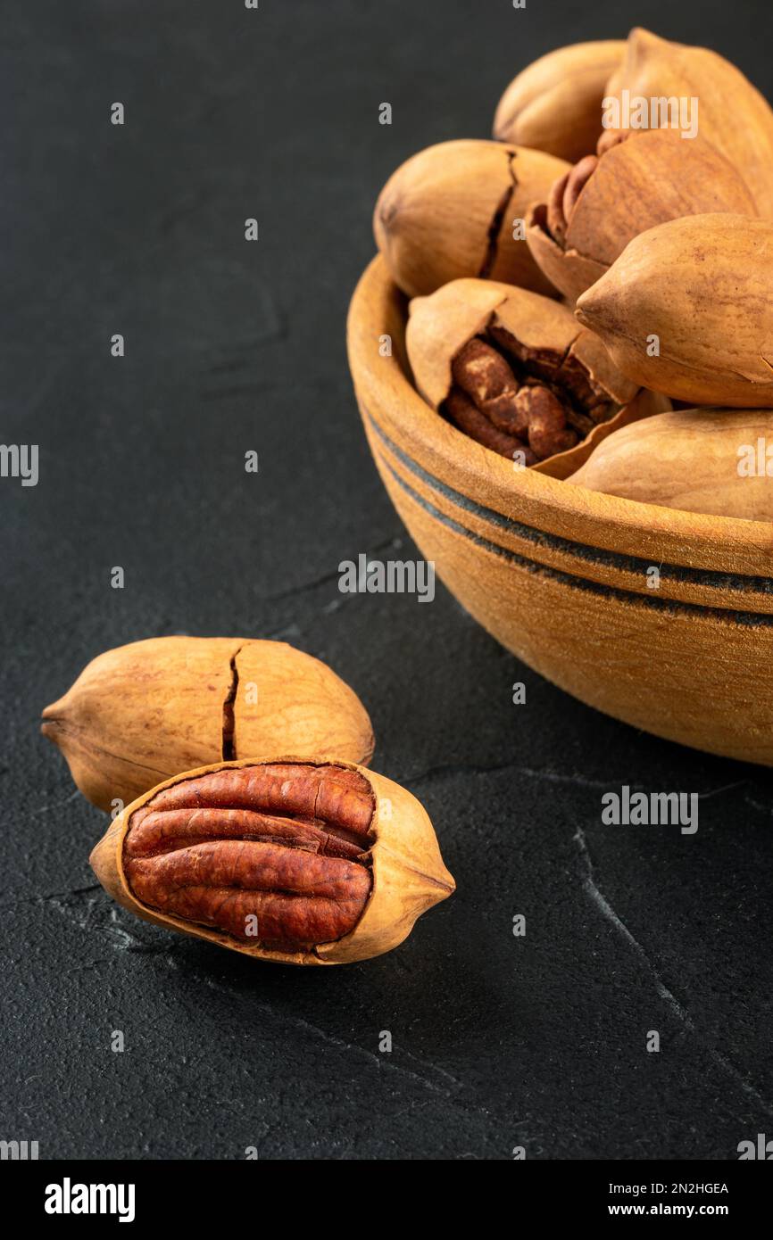 Part of a wooden bowl with in-shell pecans close-up on a dark concrete background. Stock Photo