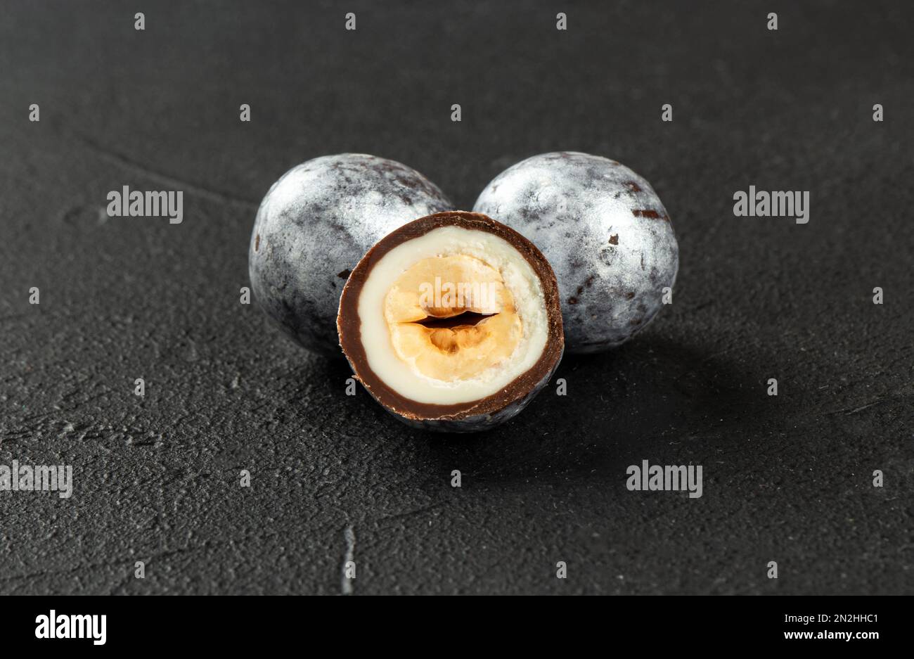 Two silver hazelnut candies in chocolate with a cut half close-up on a dark concrete background. Stock Photo