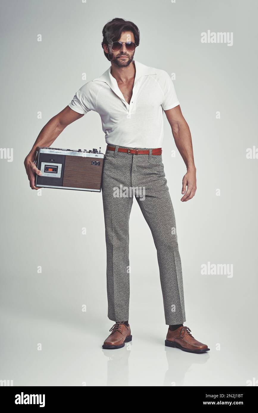 Stepping out with his tunes - 70s style. A studio shot of a handsome man in retro 70s wear holding a cassette player. Stock Photo