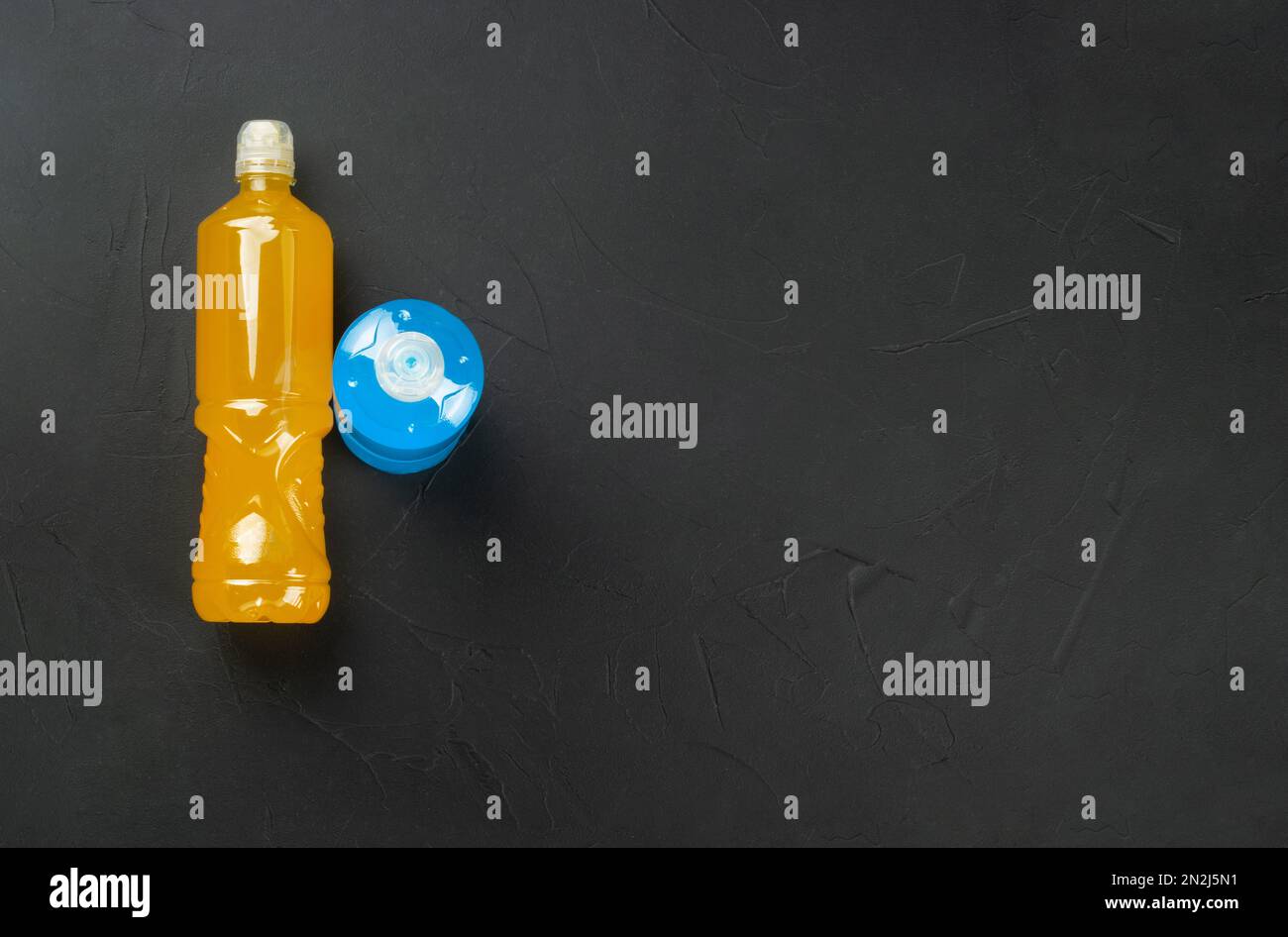 Two plastic bottles with blue and orange isotonic drinks on a dark concrete background. copy space. Top view Stock Photo