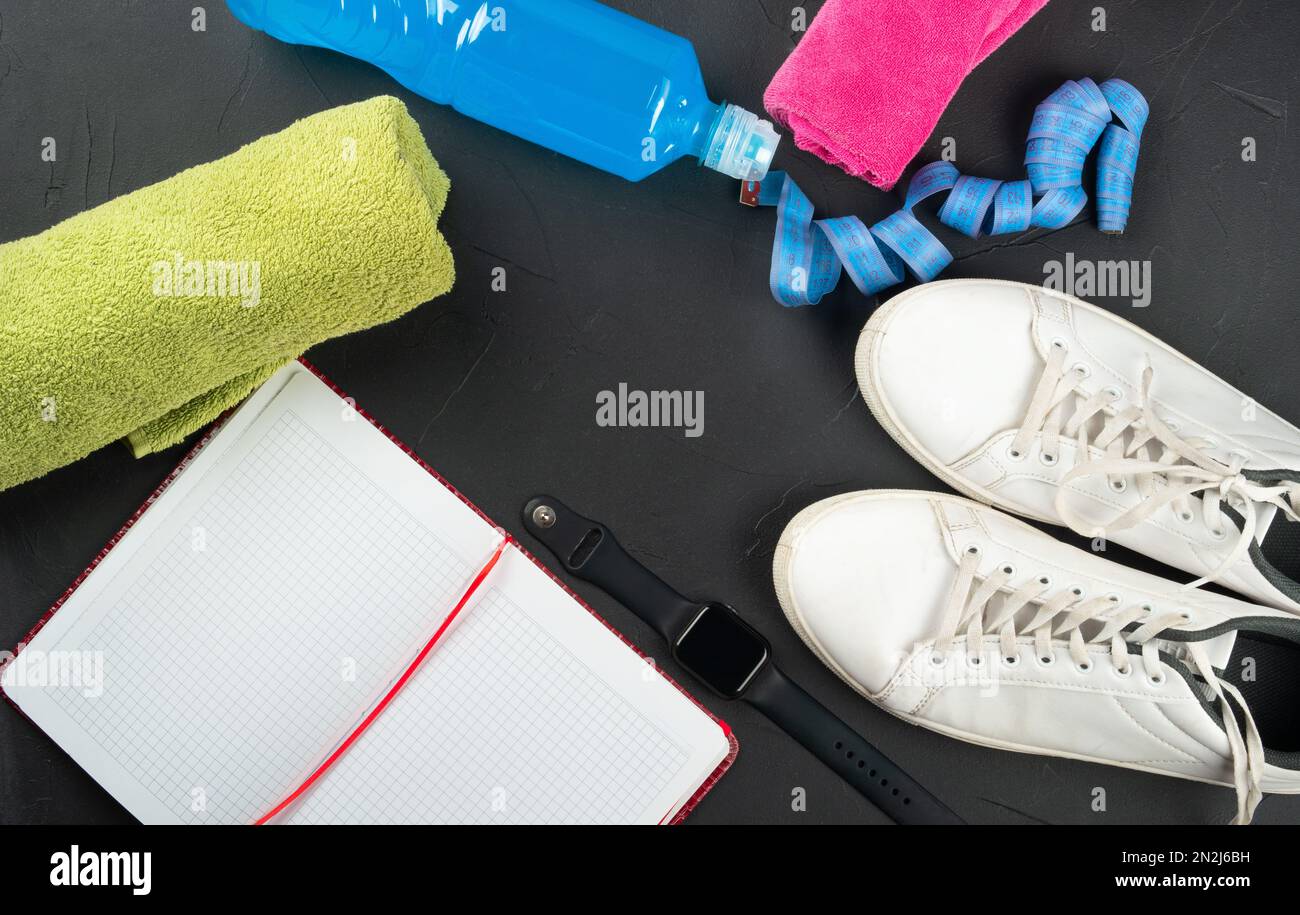 Fitness concept. Towel, sneakers, a bottle of isotonic drink, notepad, smart watch, measuring tape on a dark concrete background, top view. copy space Stock Photo