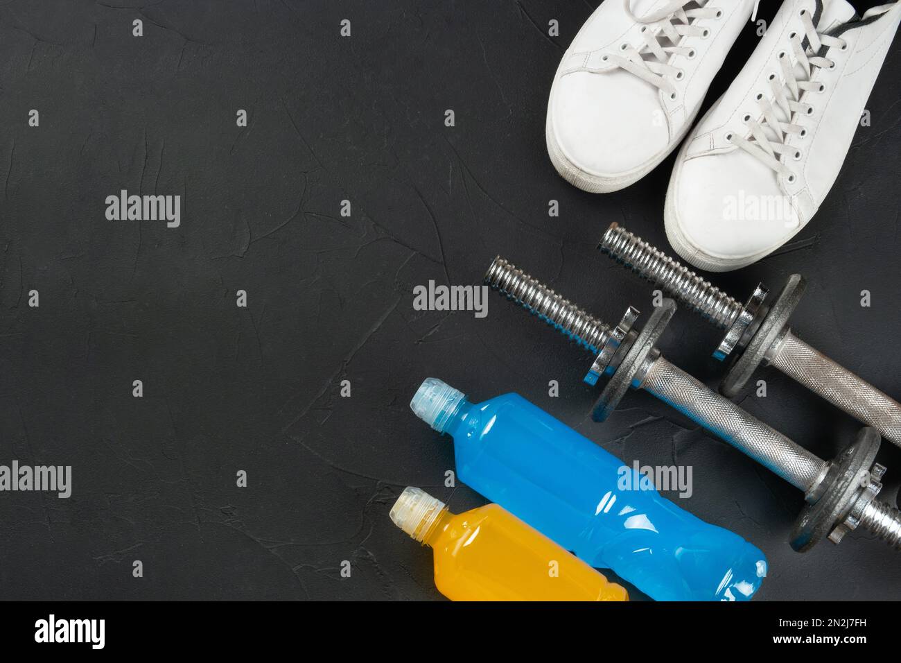 Fitness concept. Two bottles of isotonic to drink, white sneakers and dumbbells on a dark concrete background. copy space. Stock Photo