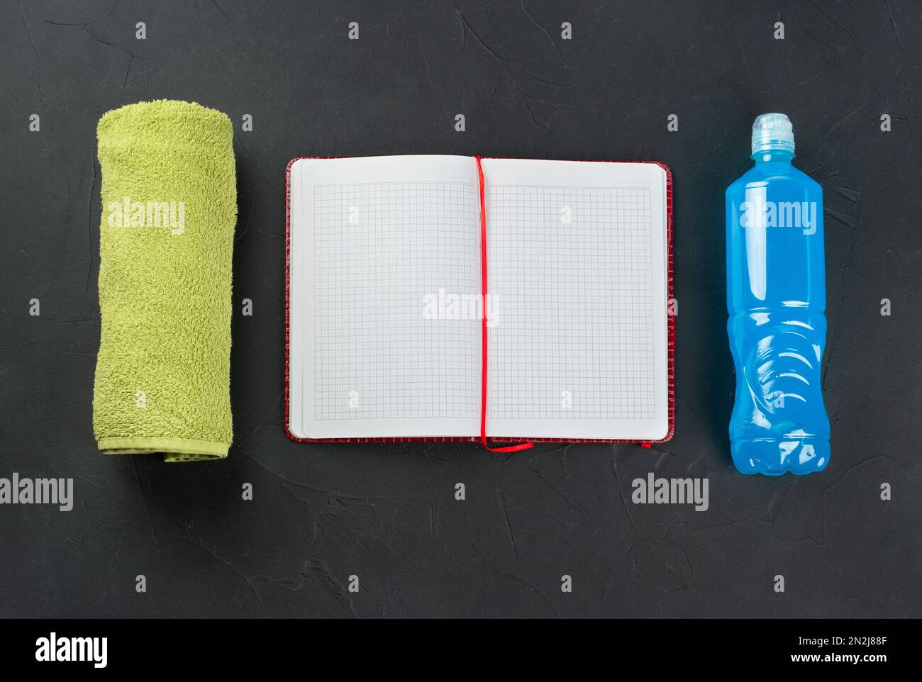 Fitness concept. Green towel with sport isotonic for drinking and open notepad, top view. Stock Photo