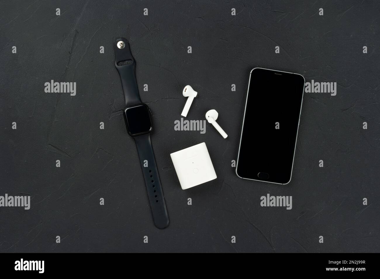 Fashion gadgets, mobile phone, smart watch and wireless headphones on a dark concrete background, top view. Stock Photo
