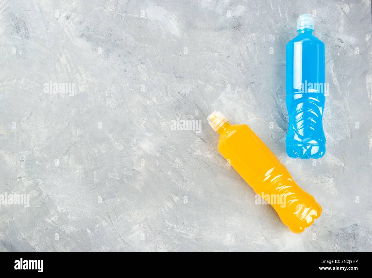 Two plastic bottles and blue and orange isotonic drinks on a light background, top view, copy space. Stock Photo