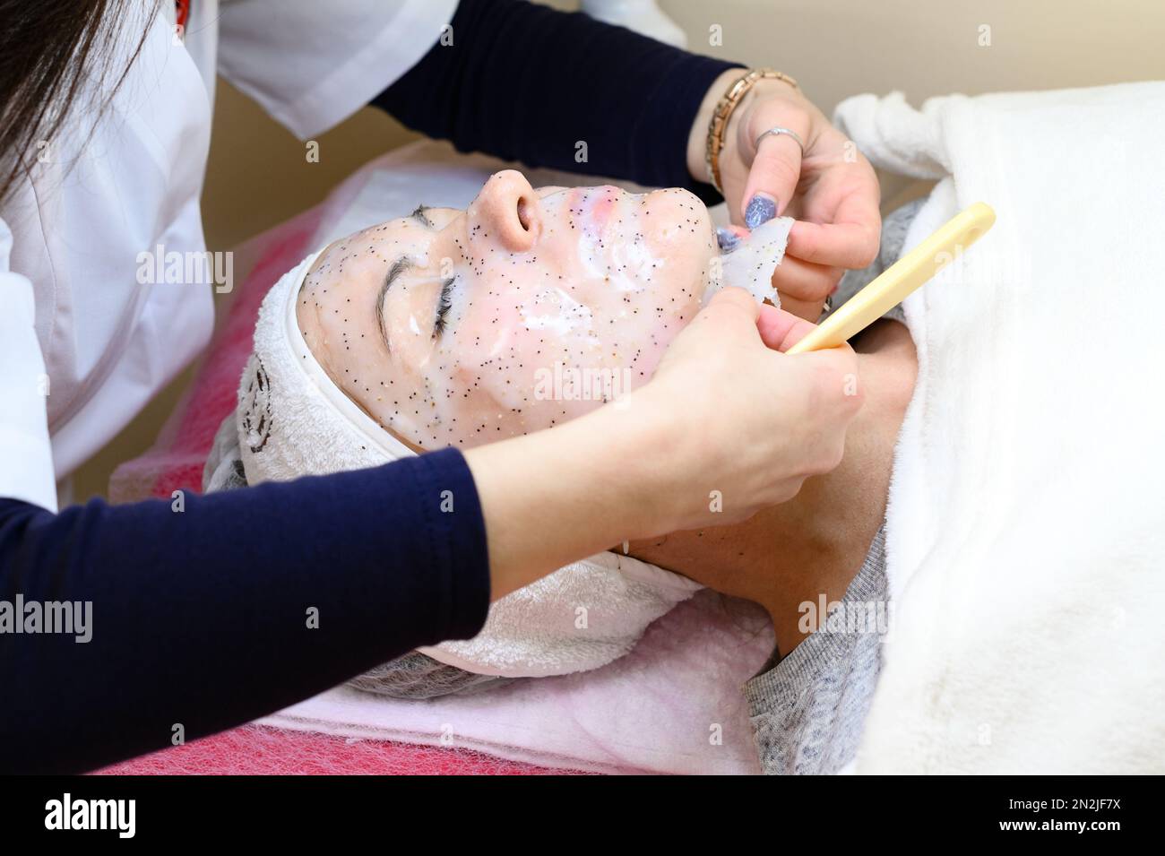 A beautician removes a moisturizing sheet mask on a woman's face with a