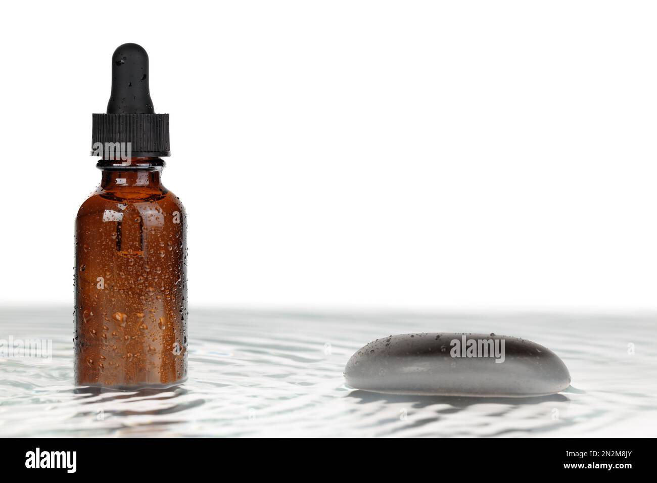 A model for a simple, zen-inspired bottle that has a dropper. Water, black stones, and skin moisture notion of natural equilibrium. Stock Photo
