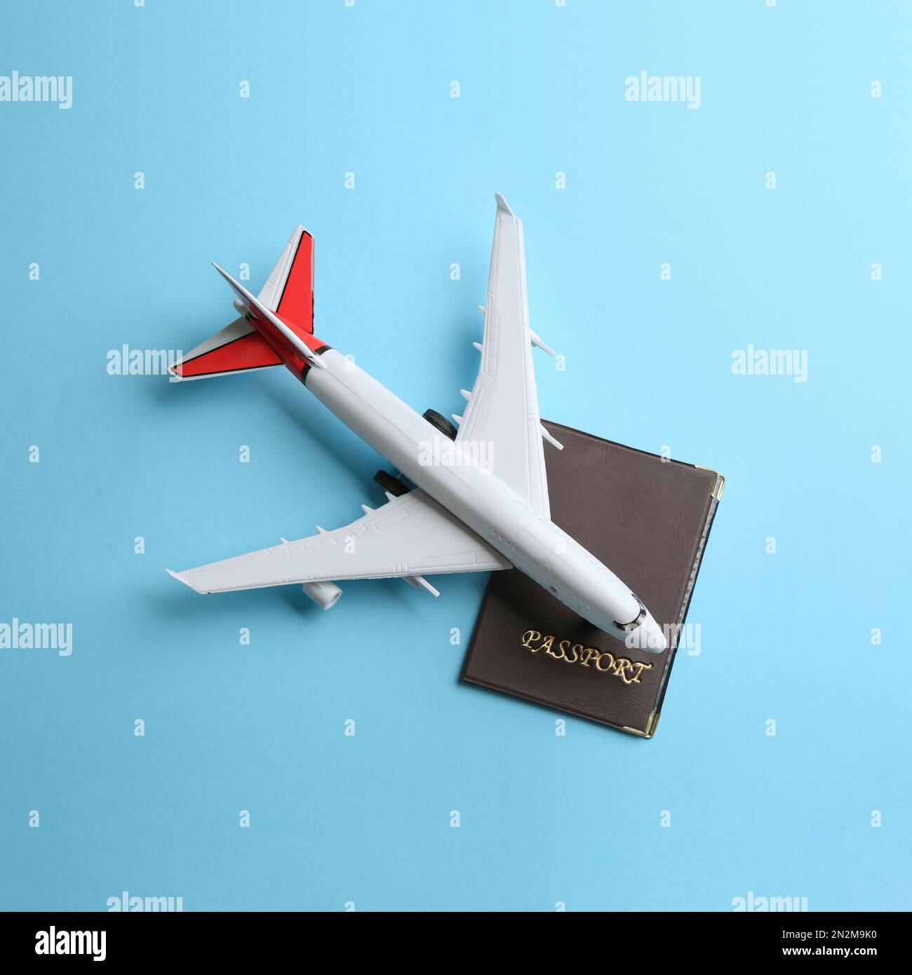 Toy airplane and passport on light blue background, flat lay Stock Photo