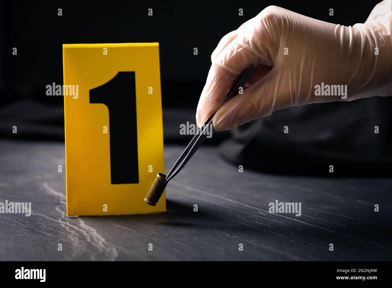 Woman taking shell casing near evidence marker at black slate table ...