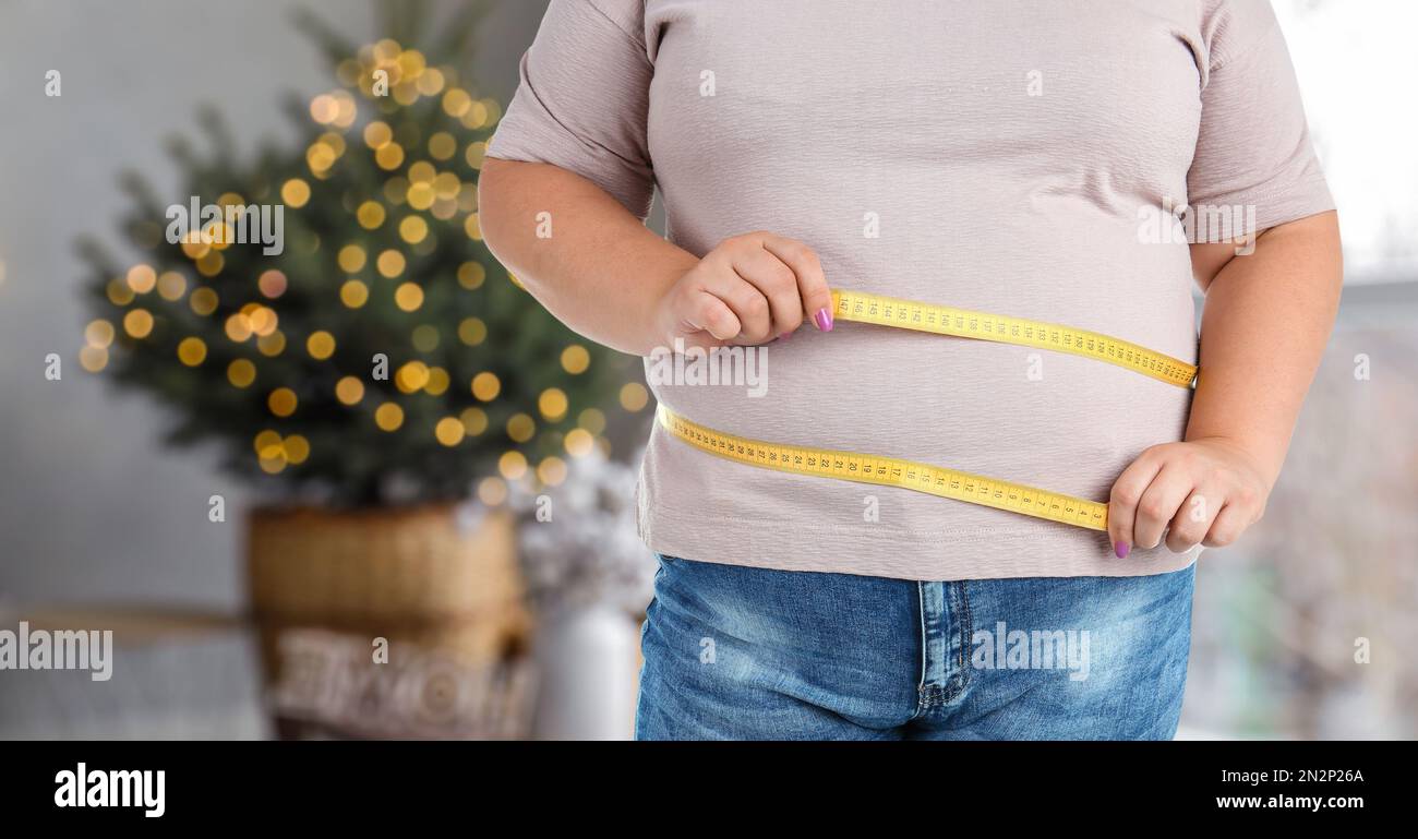 Overweight woman measuring her waist in room decorated for Christmas after holidays, closeup Stock Photo