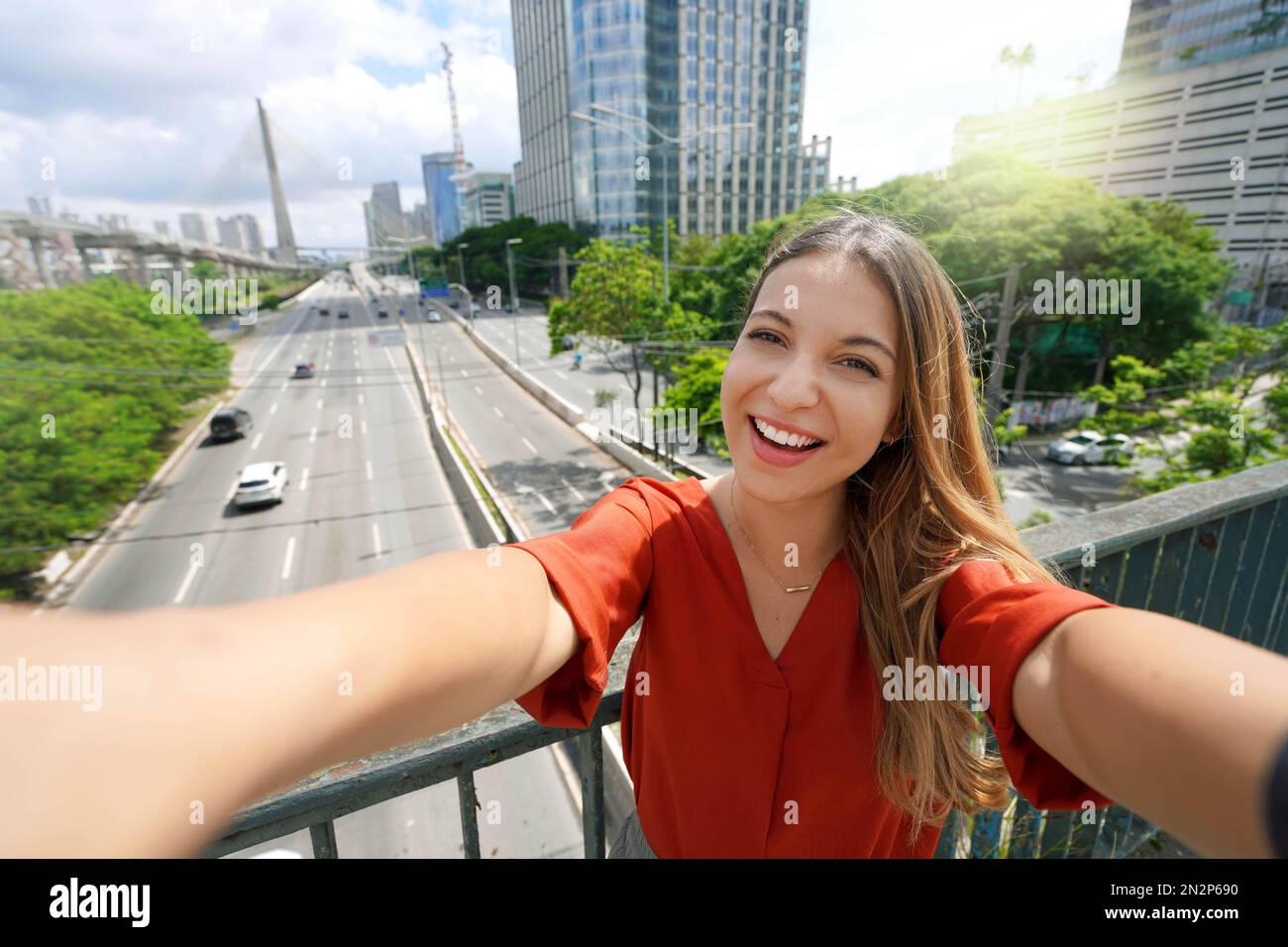 Tourism in Sao Paulo. Beautiful smiling girl takes self portrait with Ponte Estaiada bridge in Sao Paulo metropolis, Brazil. Stock Photo