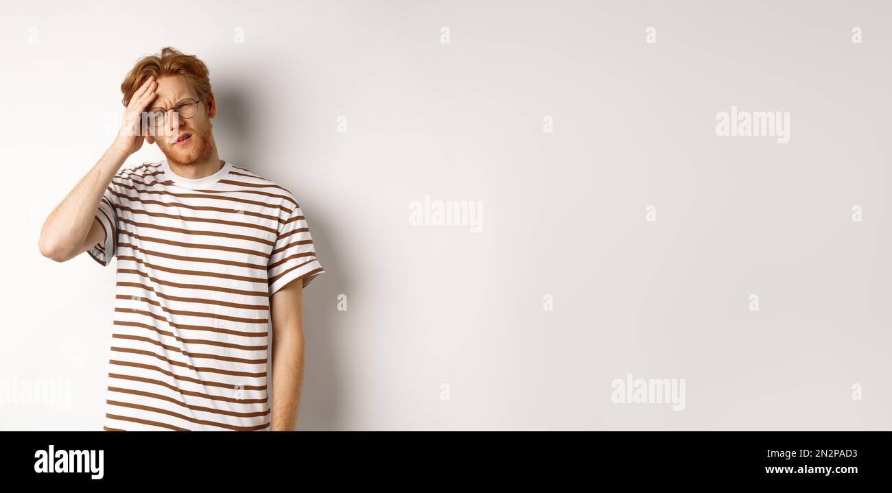 Tired young man student touching head, looking complex and tired, standing over white background Stock Photo