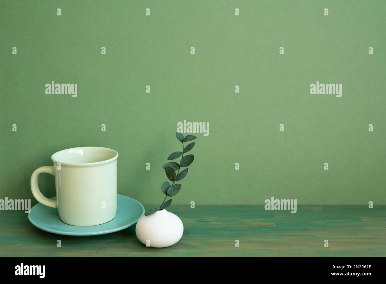 Coffee cup and eucalyptus leaf on wooden table. green wall background. minimal, copy space Stock Photo