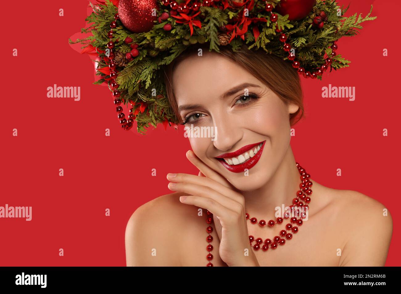 Beautiful young woman wearing Christmas wreath on red background, closeup Stock Photo