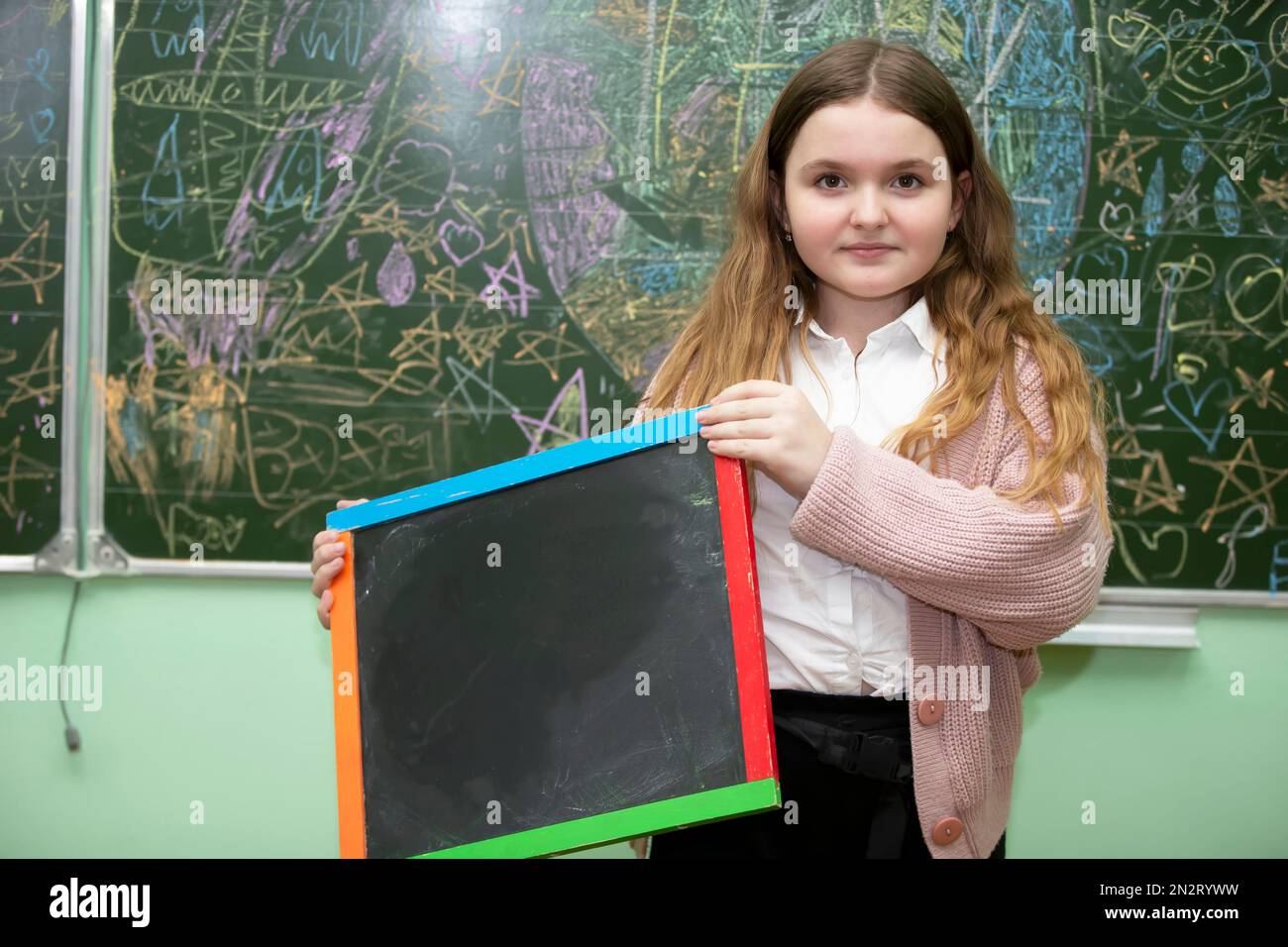 Schoolgirl of middle school age in the classroom holding a drawing board and looking at the camera. Stock Photo