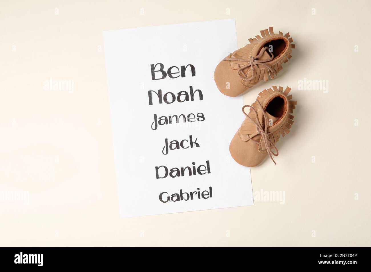 List of baby names and child's shoes on beige background, flat lay