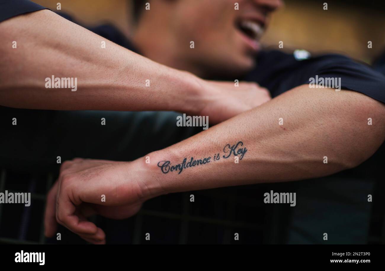 A tattoo reading Confidence is Key decorates the arm of New York Yankees' Tyler  Wade as he hangs over the dugout rail before the start of an exhibition  spring training baseball game