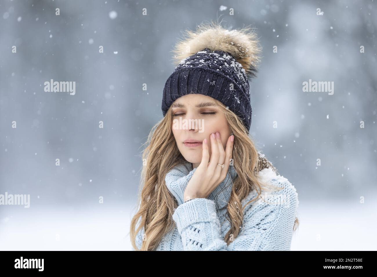 A young woman has a toothache outside in winter weather, she has sensitive enamel to the cold. Stock Photo