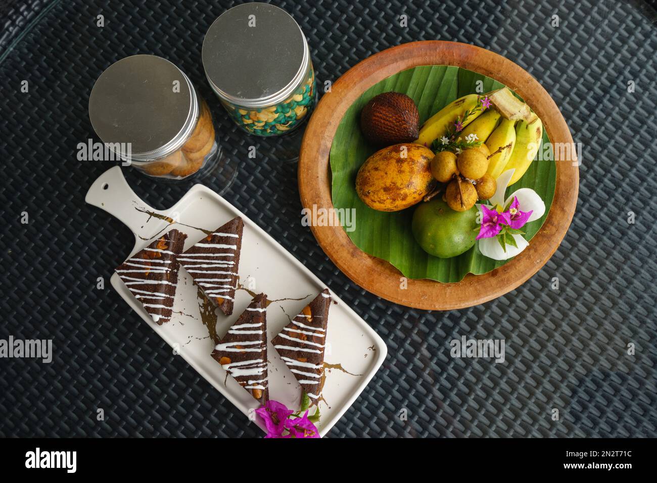 Overhead view of slices of chocolate cake, fresh fruit and jars of biscuits and snacks Stock Photo