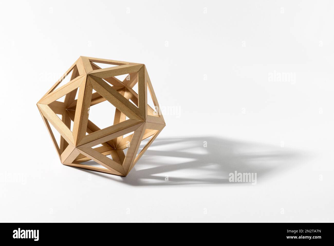 Platonic solid icosahedron shape made of light wood casting shadow on gray background Stock Photo