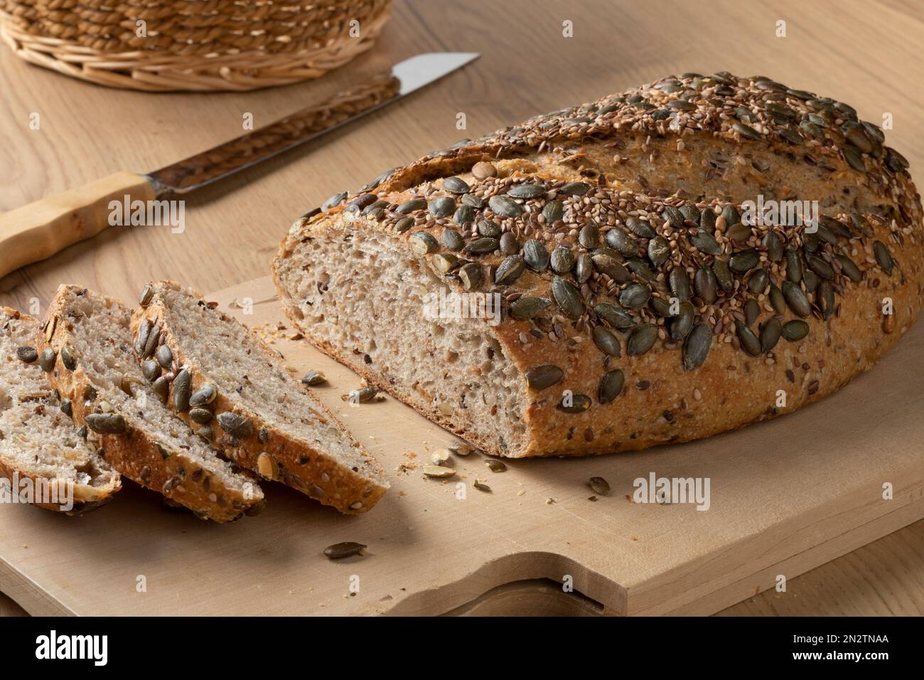 Fresh loaf and slices of spelt bread and a variety of seeds on top close up on a cutting board Stock Photo