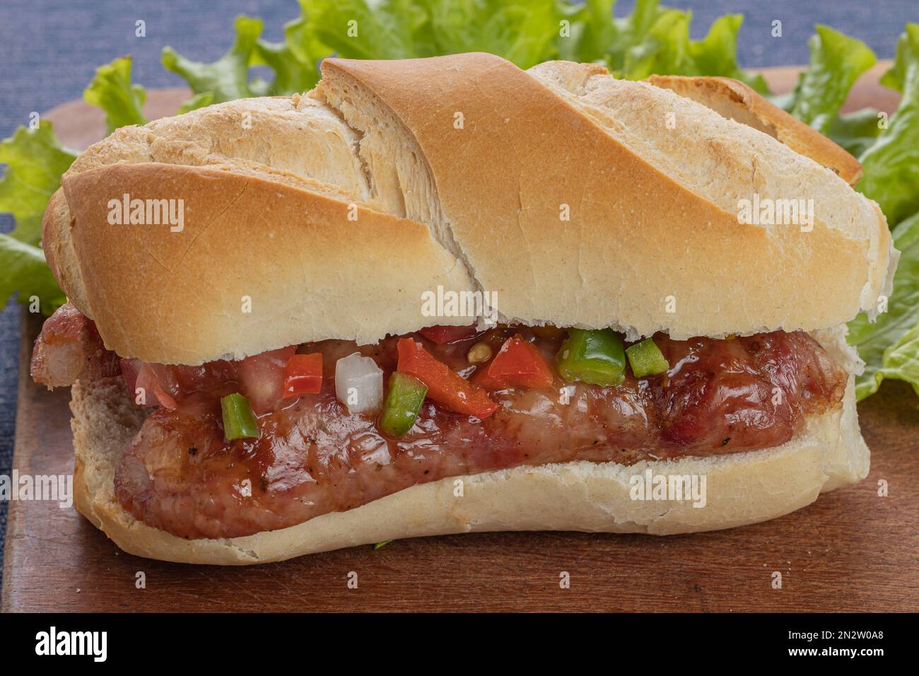 Close up of a choripan, typical argentine sandwich with chorizo and creole sauce on a wooden board. Stock Photo