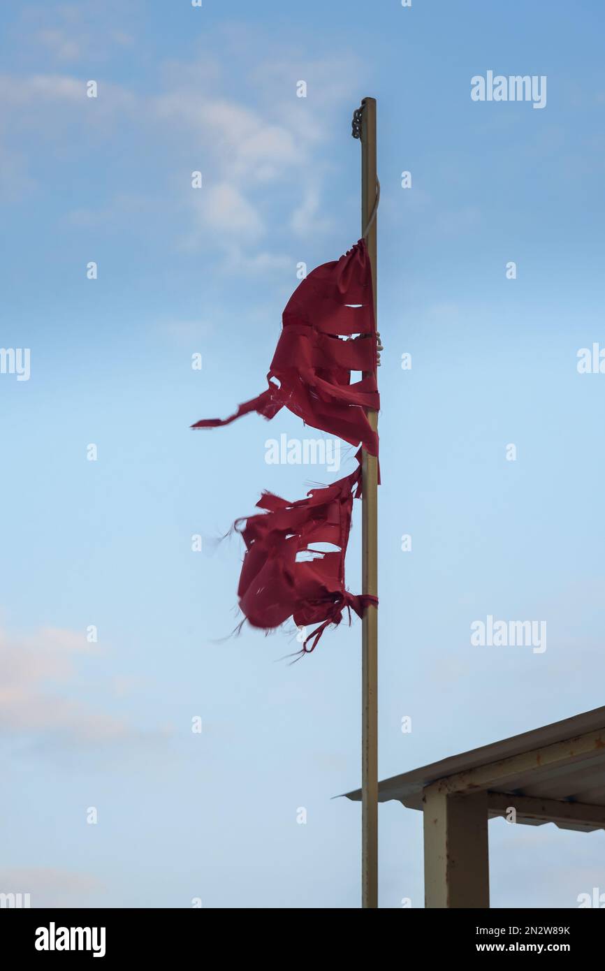 Old tattered red flag in wind in front of the blue sky Stock Photo