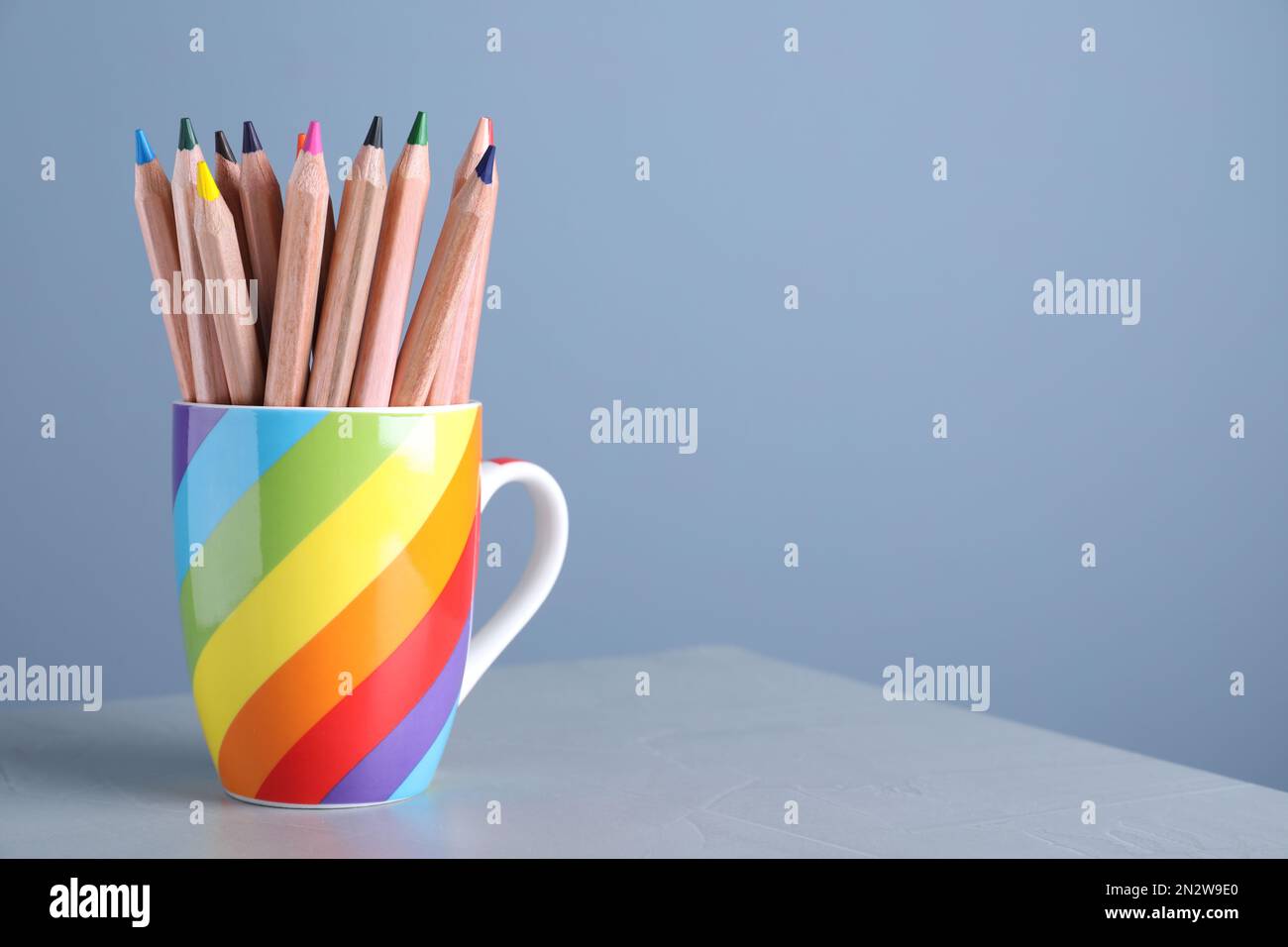 Colorful pencils in cup on grey table against light blue background. Space for text Stock Photo