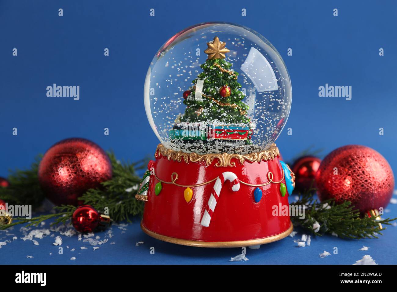 Beautiful snow globe, Christmas balls and coniferous twigs on blue background Stock Photo
