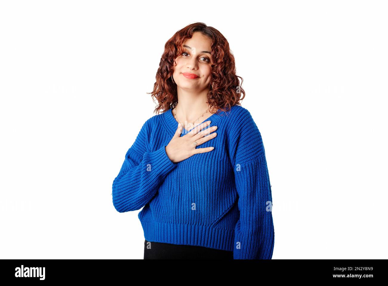 Portrait of young woman wearing knitted sweater standing isolated over white background touching chest with her palm, smiles tenderly and looks at the Stock Photo