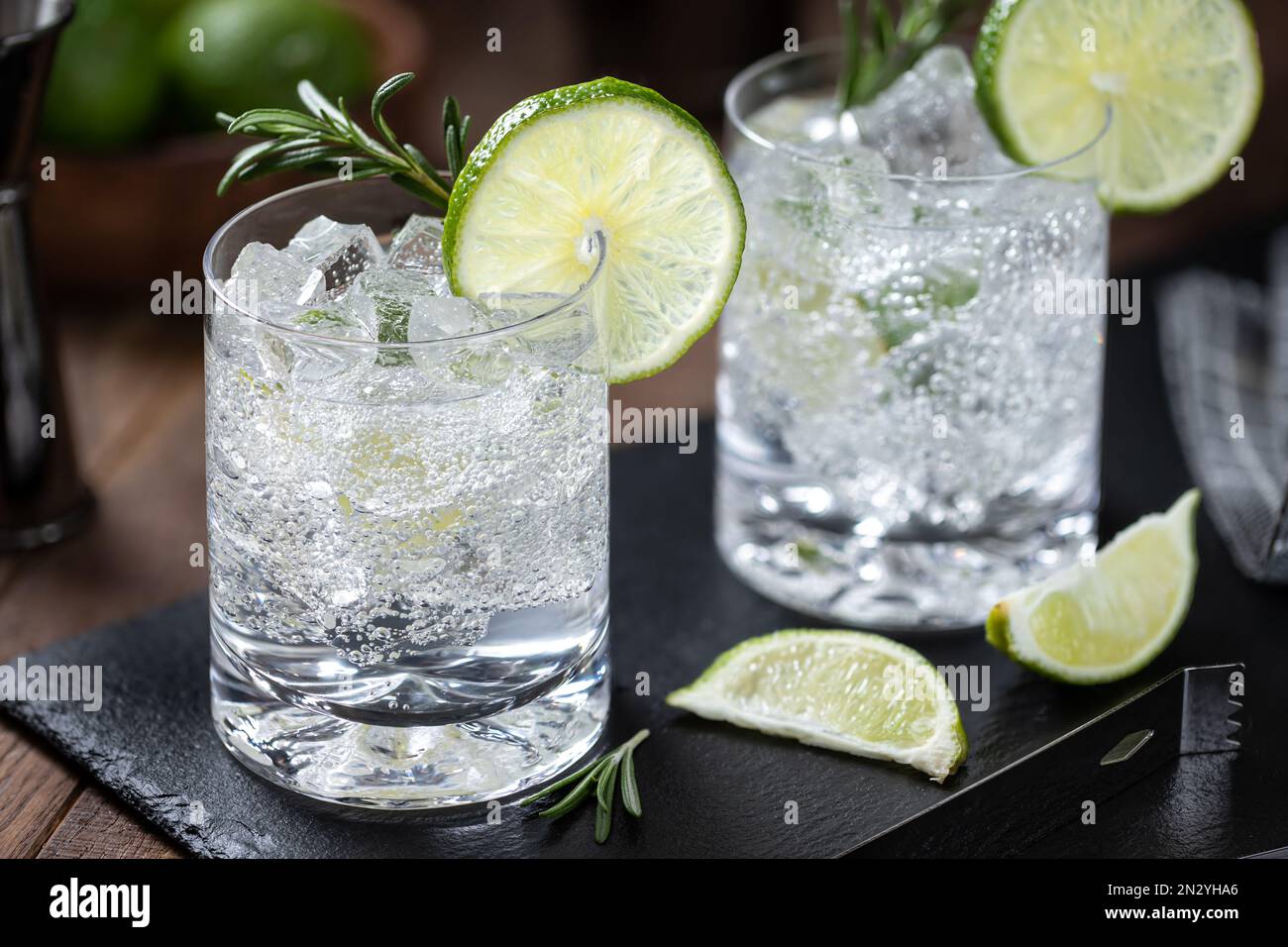 Gin and tonic cocktail drink with lime slices, rosemary and ice on a black slate board Stock Photo