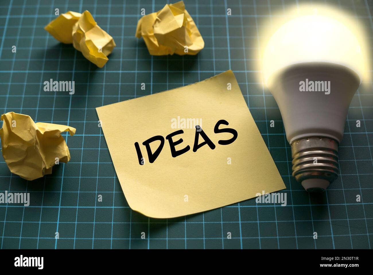 Ideas concept with a bright bulb and yellow memo note on a green craft mat. Stock Photo