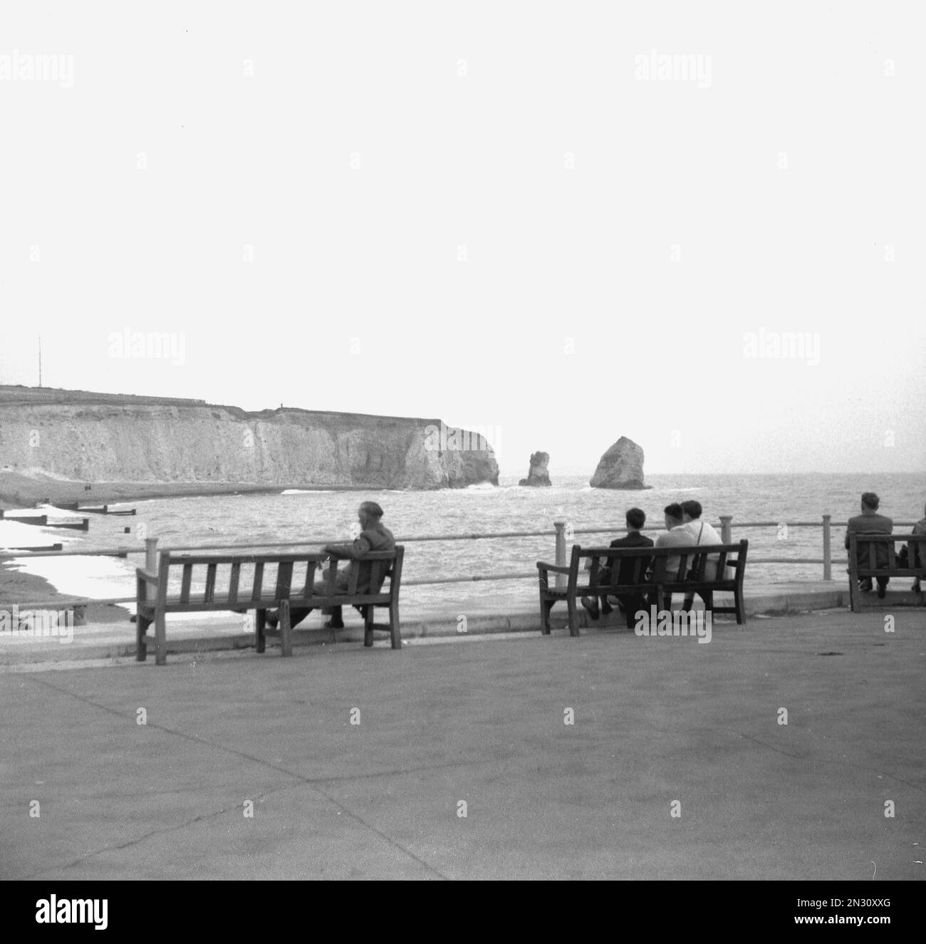 1950s, historical, visitors sitting on benches at the coast at Freshwater Bay, nr Lymington, Isle of Wight, Hampshire, England UK. Stock Photo