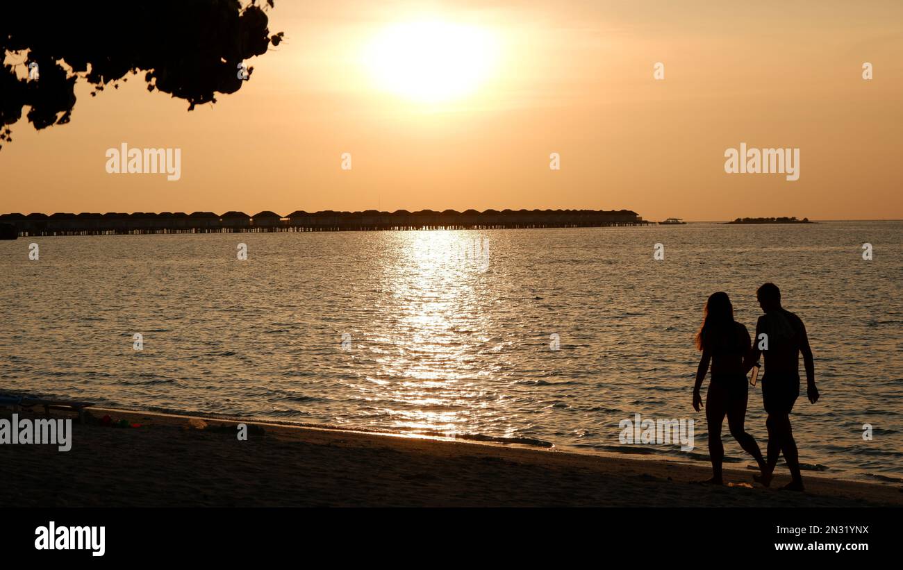 Couple walking on the beach with a sunset backdrop Stock Photo - Alamy
